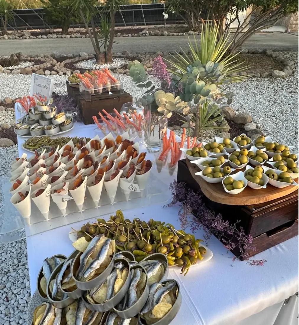 Mesa de catering de El Hogar montada al aire libre con conos de embutido, encurtidos y aceitunas