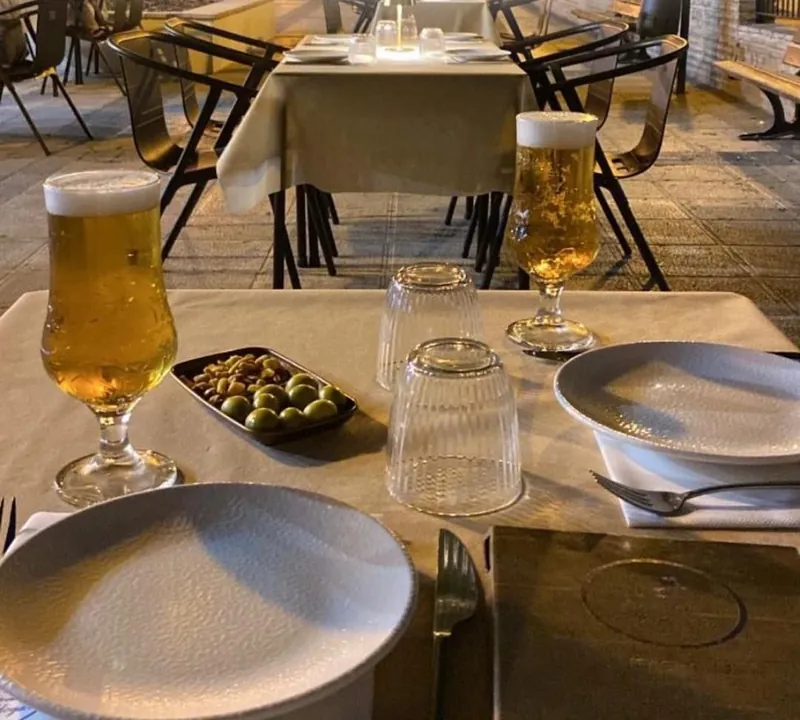 Mesa preparada en la terraza de El Hogar por la noche, con cervezas y aperitivo de aceitunas